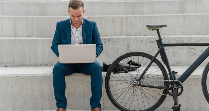 ein Mann mit einem Laptop auf dem Schoß neben seinem Jobrad